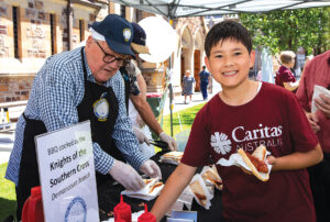 David Lloyd from Knights of the Southern Cross (Dernancourt branch) serves Caritas ambassador Leonardo Dos Santos a sausage during the post-service barbecue.